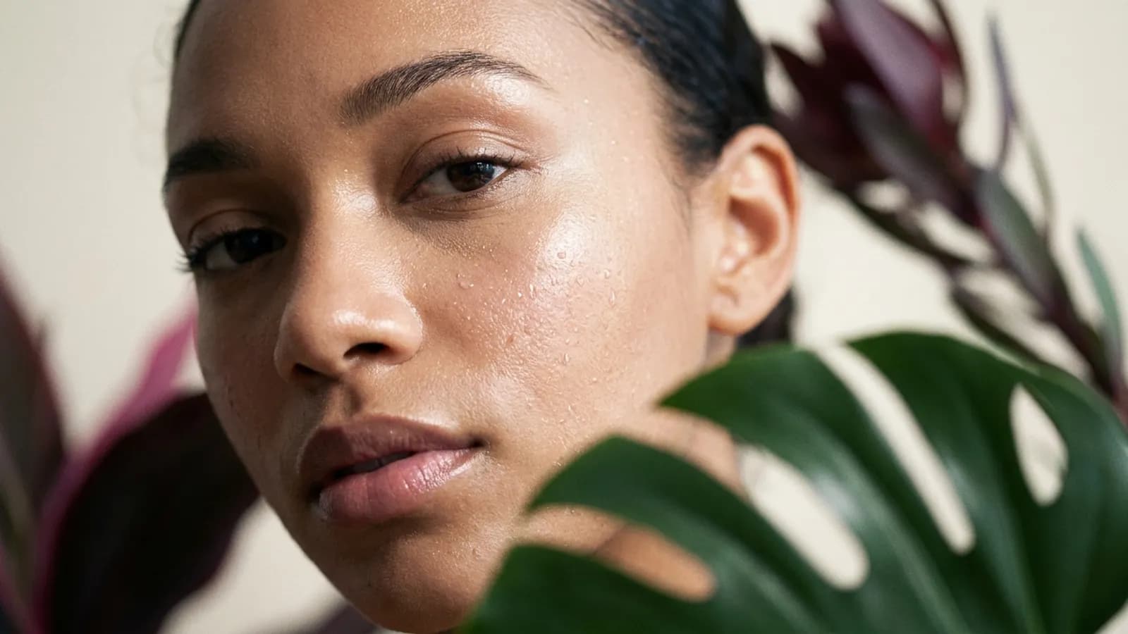 Gros plan sur un visage à la peau lumineuse, feuille de monstera en avant-plan